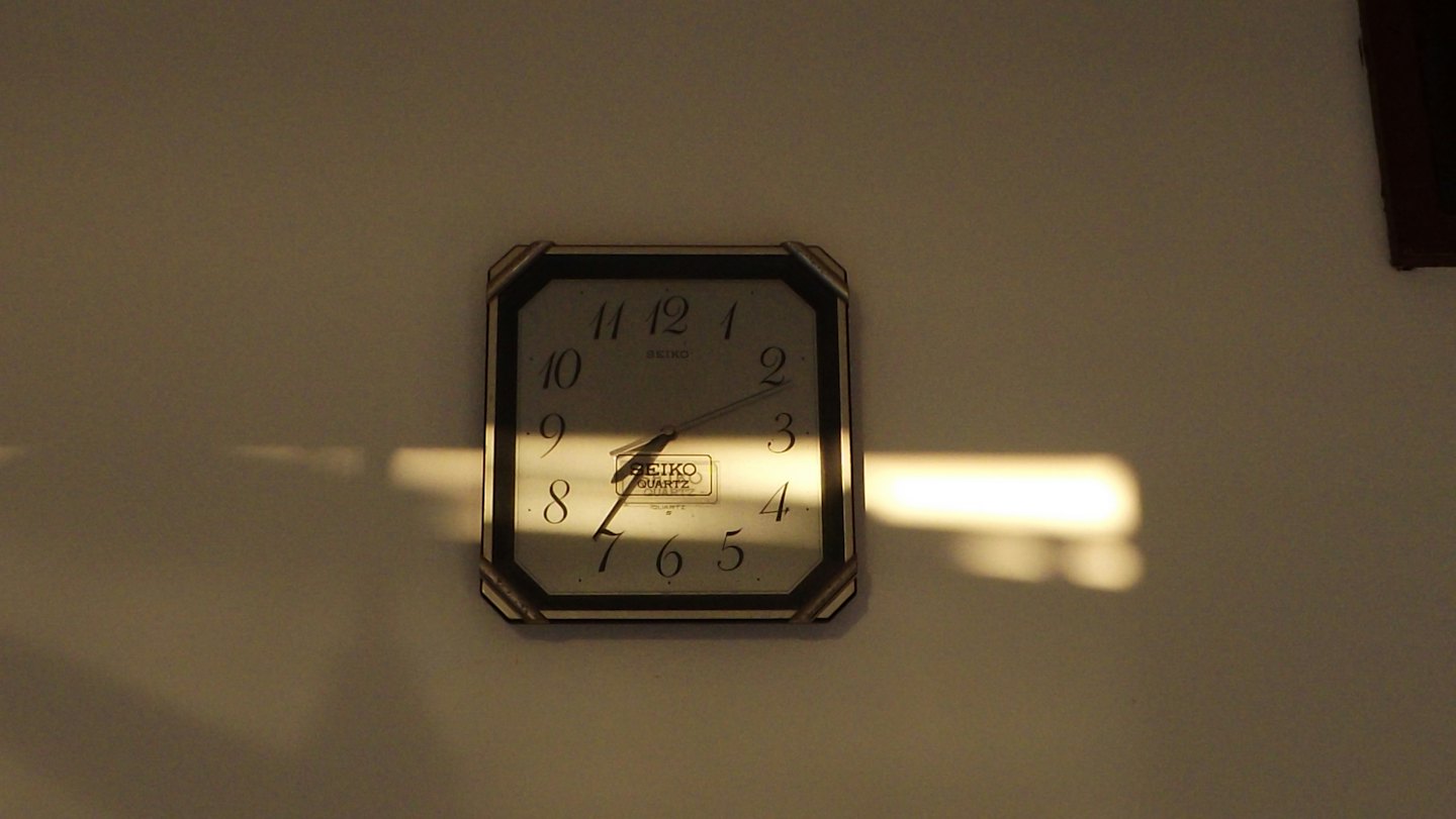 Un reloj de pared octogonal cuelga en una pared lisa.
