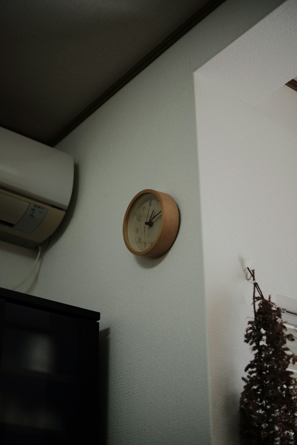 Reloj de pared de madera minimalista colgado en una pared blanca texturizada.