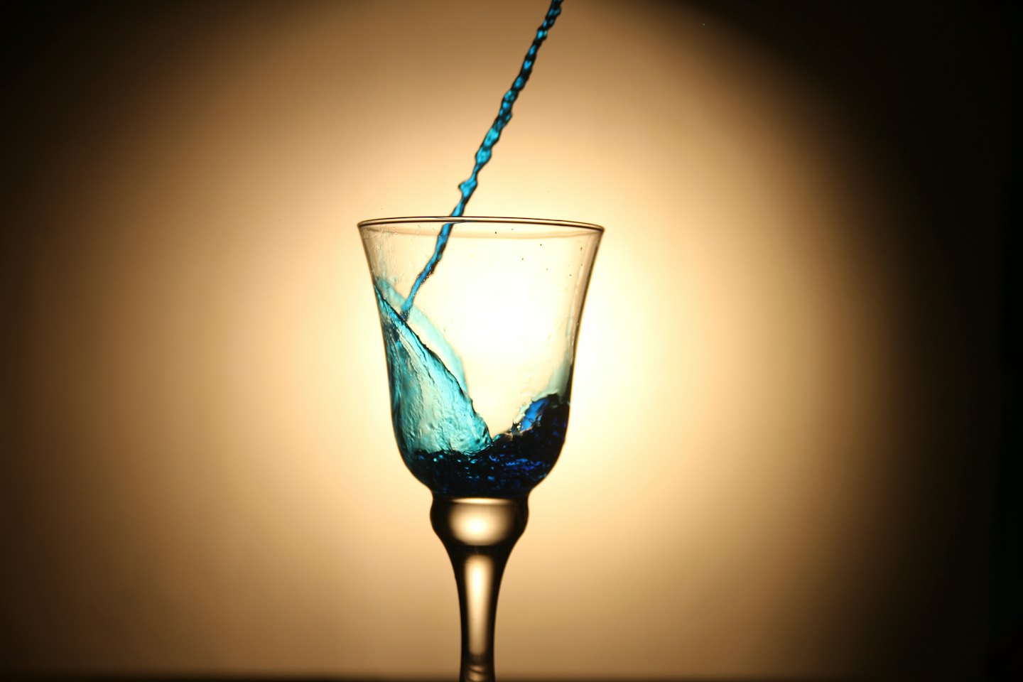 Líquido azul salpicando en una copa de cristal transparente.