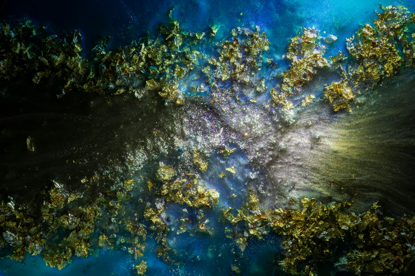 Líquido azul oscuro con escamas doradas y purpurina plateada.